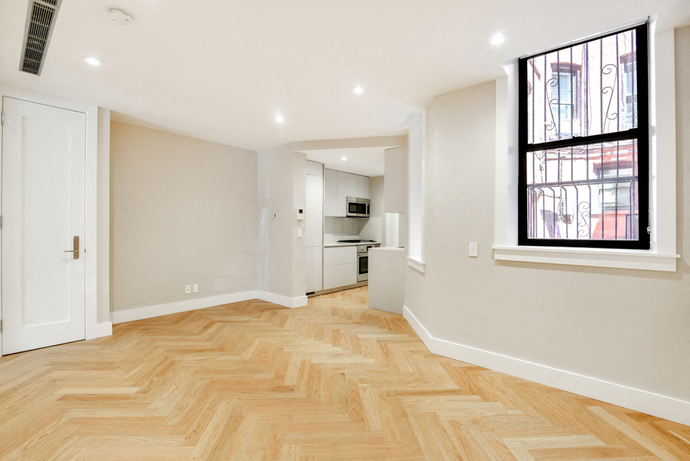the living room and kitchen of an apartment with wood flooring and a large window